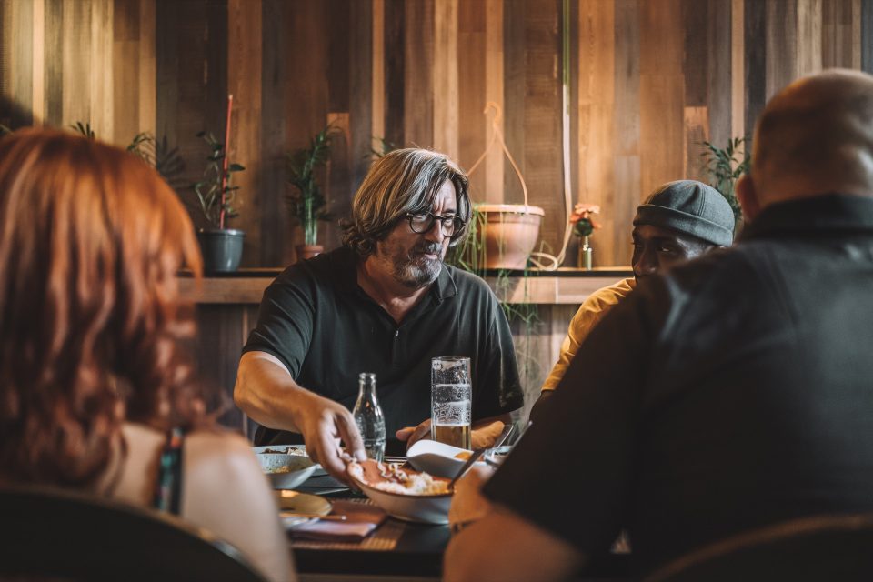 Äldre man med glasögon äter middag med vänner vid ett bord på restaurang
